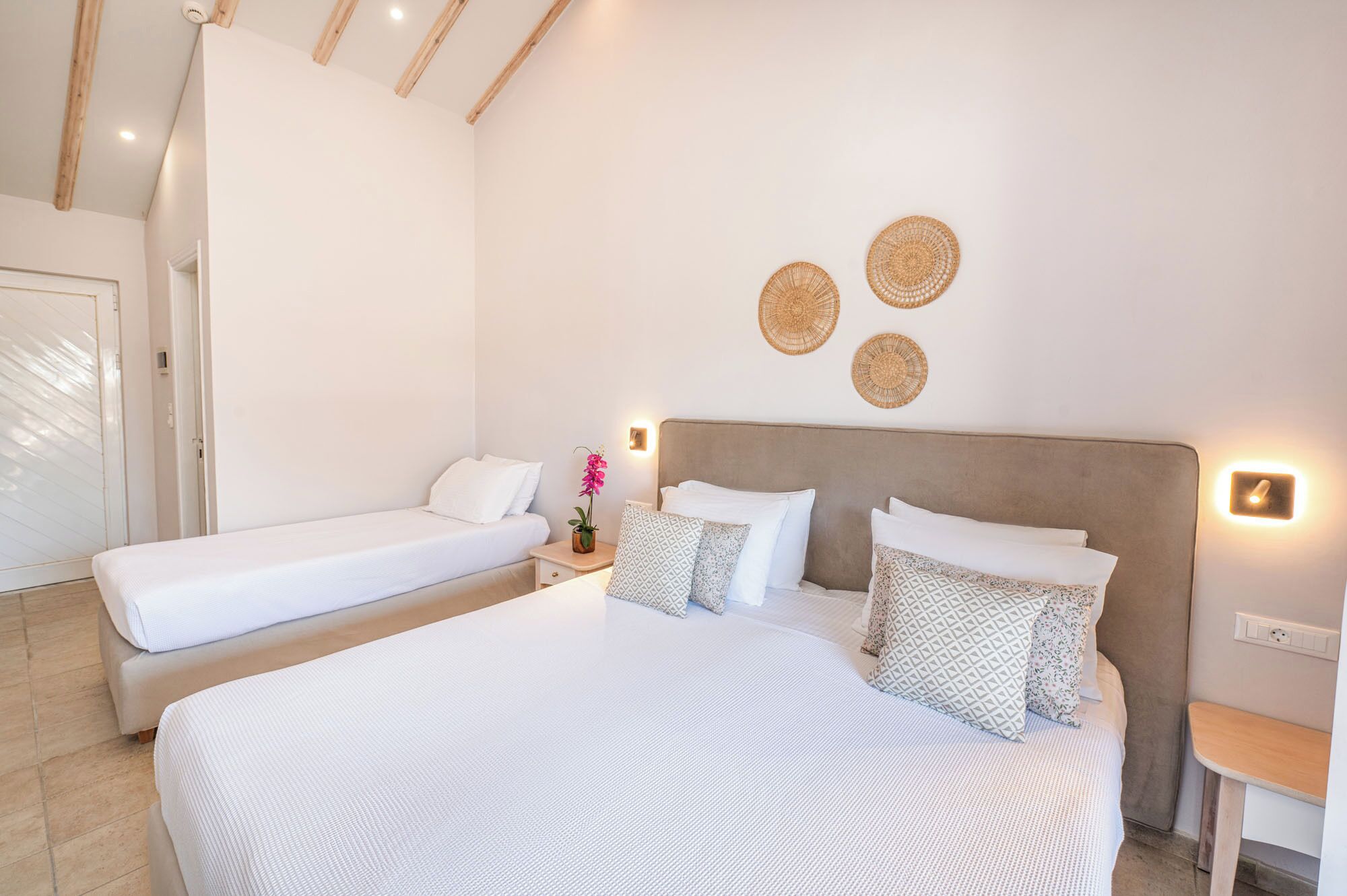 Un dormitorio con una cama grande, dos camas individuales, una mesita de noche con lámpara y un aplique de pared.