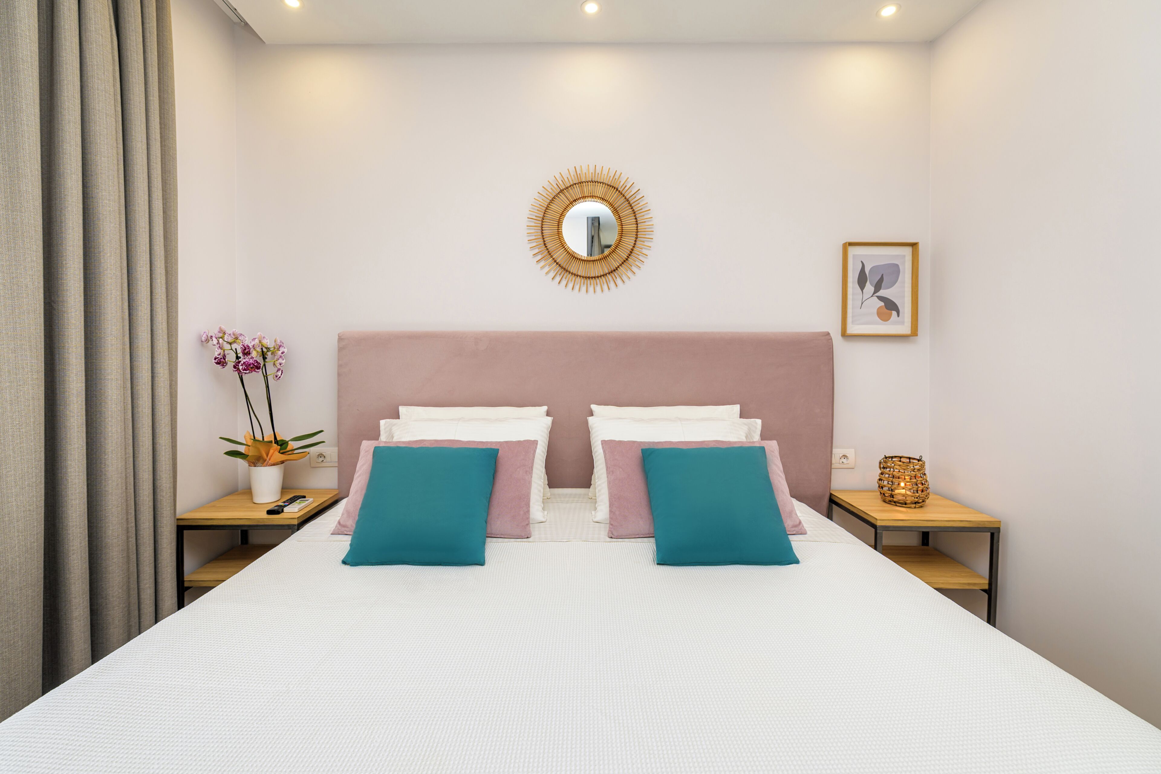 A neatly arranged hotel room with a large bed, two bedside tables, a wall-mounted mirror, and a framed picture.