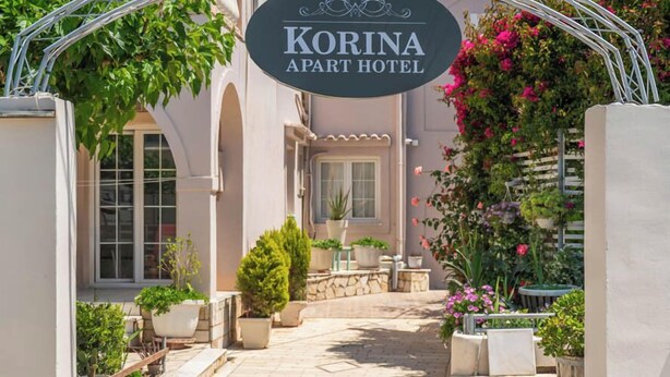 The entrance to the Korina Apartment Hotel, featuring a clear pathway, potted plants, and a sign above the entrance. - Korina Apart Hotel (Corfu)