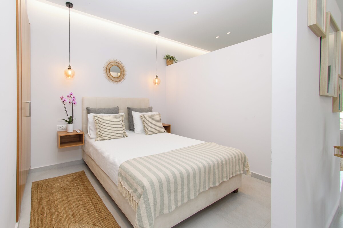 A bedroom with a bed, bedside tables, a mirror, and hanging lights.