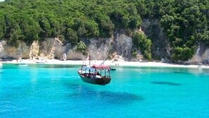 A boat on clear turquoise water with a rocky coastline and white sandy beach in the background. - Korina Apart Hotel (Corfu)