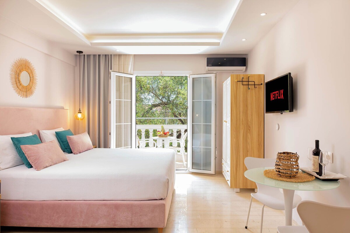 A bedroom with a bed, a TV, a table with a bottle and glasses, and a balcony with a view.