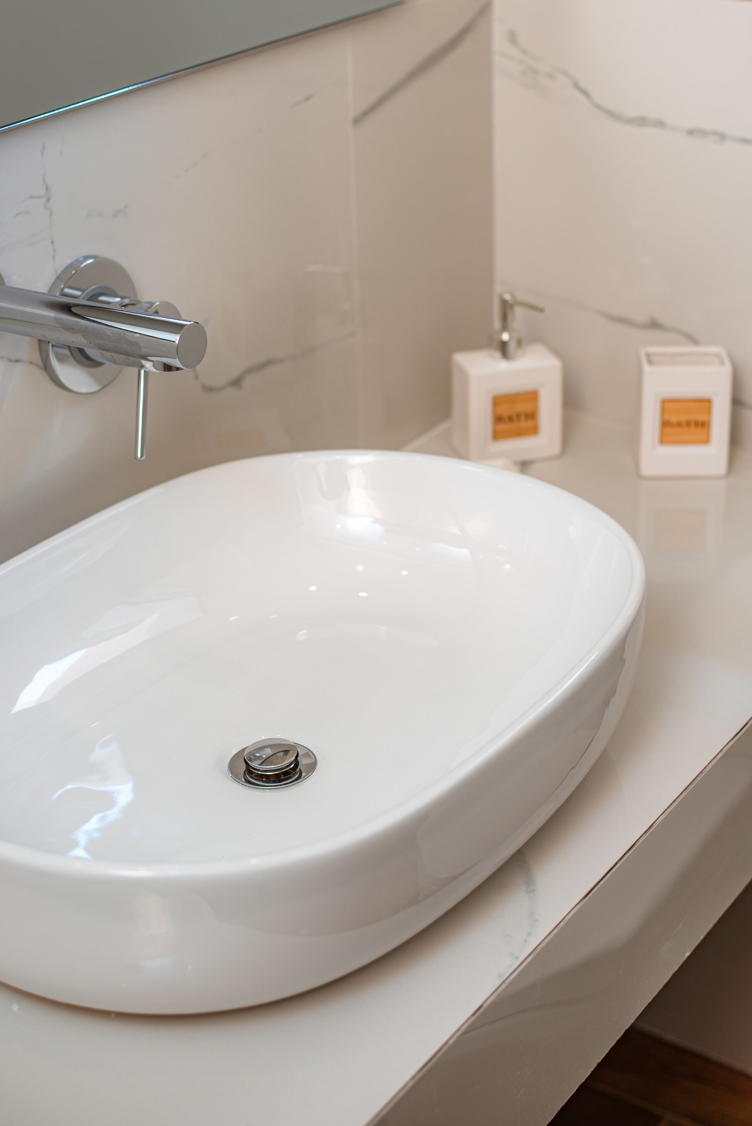 Un lavabo de bany de color blanc amb un aixeta cromada, un mirall a la part superior i dos dispensadors de sabó a la superfície del taulell.