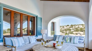 A cozy outdoor seating area with a round wooden table, a sofa, and a view of a hillside. - La Mar - By Almarina Villas (BENISSA)