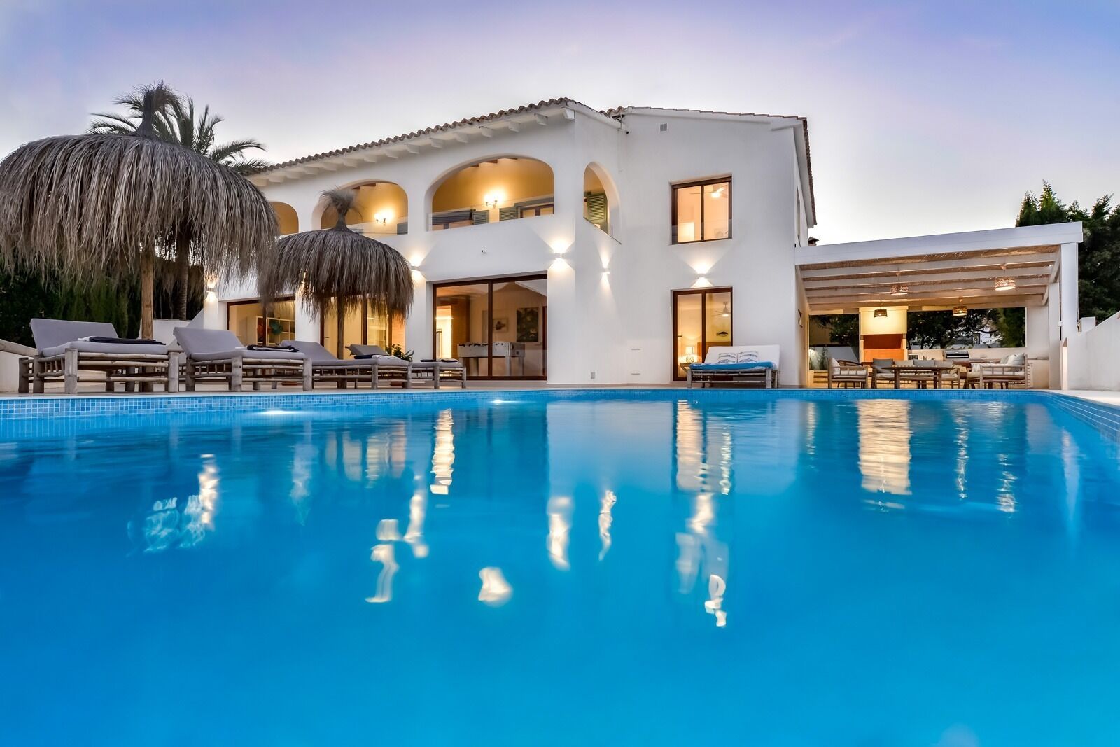 Eine moderne Villa mit Schwimmbad, Sitzgelegenheit im Freien und einer gut beleuchteten Einfahrt.