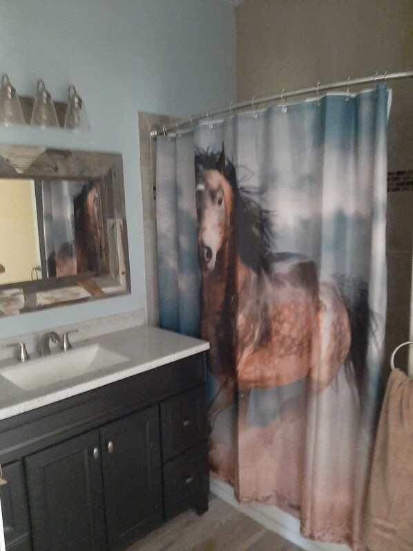 A bathroom with a large mirror, a sink, and a shower curtain depicting a horse.