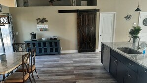 A kitchen with a wooden floor, a dining table with chairs, a coffee station, and a sliding barn door.