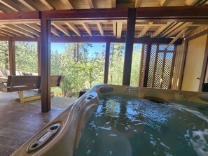 Un jacuzzi bajo una pérgola de madera, con un banco y vista a árboles.
