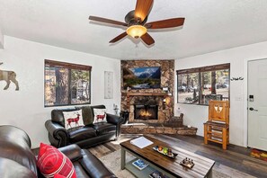 A living room with a fireplace, leather sofa, and a ceiling fan. - Slopeside Cabin A Walk to Lifts & Parking (Big Bear Lake)