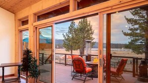 A wooden deck with a glass door leading to an outdoor area. Inside, there is a bench, a potted plant, and a table with chairs. - Lake Time Villa I Lake Views + Hot Tub (Big Bear Lake)