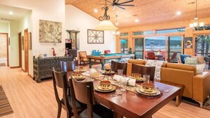 A dining area with a wooden table set for a meal, a pool table, and a sofa with a view of the outdoors. - Lake Time Villa I Lake Views + Hot Tub (Big Bear Lake)