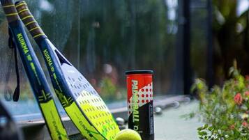 A yellow tennis ball, two tennis rackets, and a can of Pabst Blue Ribbon beer on a concrete surface.