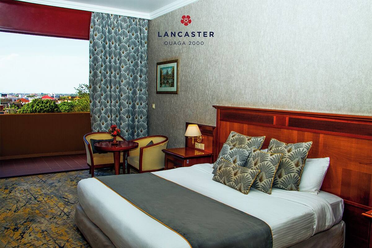 Ein Hotelzimmer mit Bett, Schreibtisch, Stuhl, Lampe und Blick auf die Stadt.