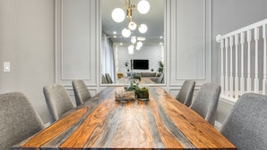 Une salle à manger avec une grande table en bois, des chaises à revêtement gris et un lustre.