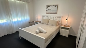 A neatly arranged bedroom with a bed, two bedside tables, a hanging light, and a painting on the wall. - Peppermint Cottage-beautiful, newly renovated holiday home property that will take your breath away (West Busselton)