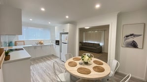 A modern kitchen with white cabinets and a dining area with a round table. - Peppermint Cottage-beautiful, newly renovated holiday home property that will take your breath away (West Busselton)