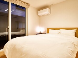 Ett hotellrum med en stor säng, ett nattduksbord, en lampa och en luftkonditioneringsanläggning.