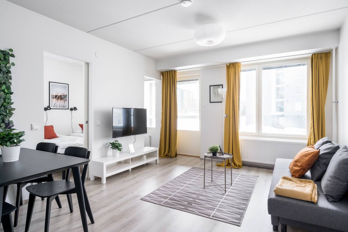 Un salon moderne avec un téléviseur à écran plat, un canapé, une table à manger avec des chaises et une plante en pot.