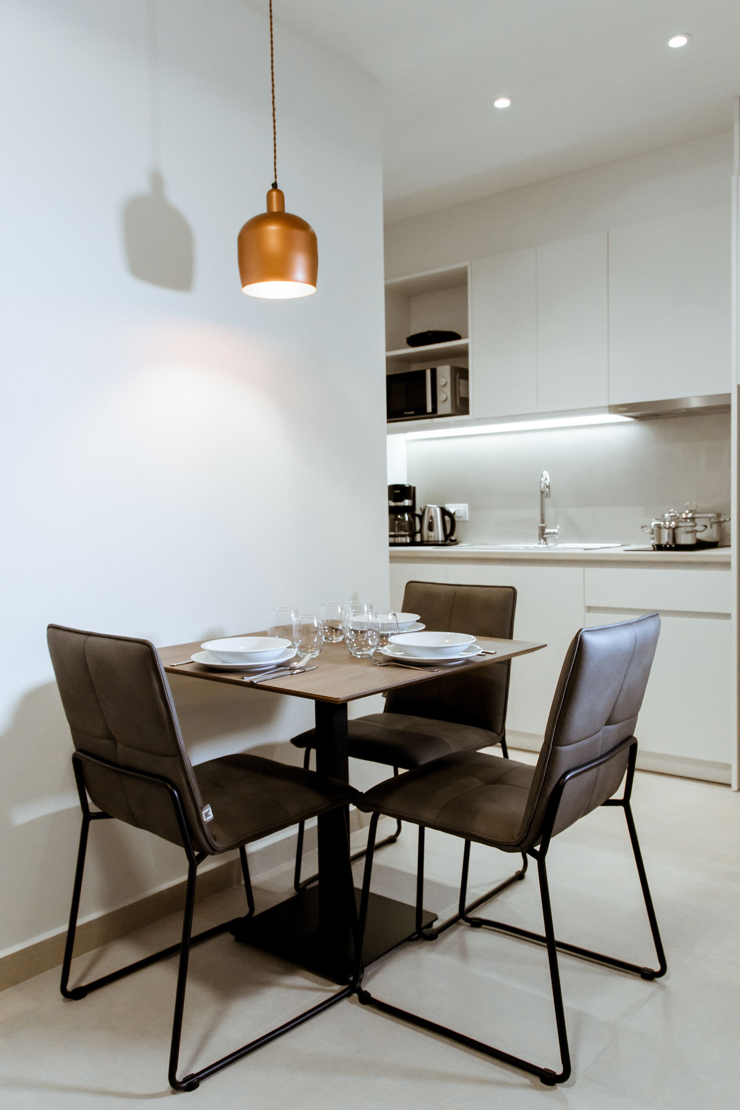 A modern dining area with a round table, four chairs, and a pendant light.