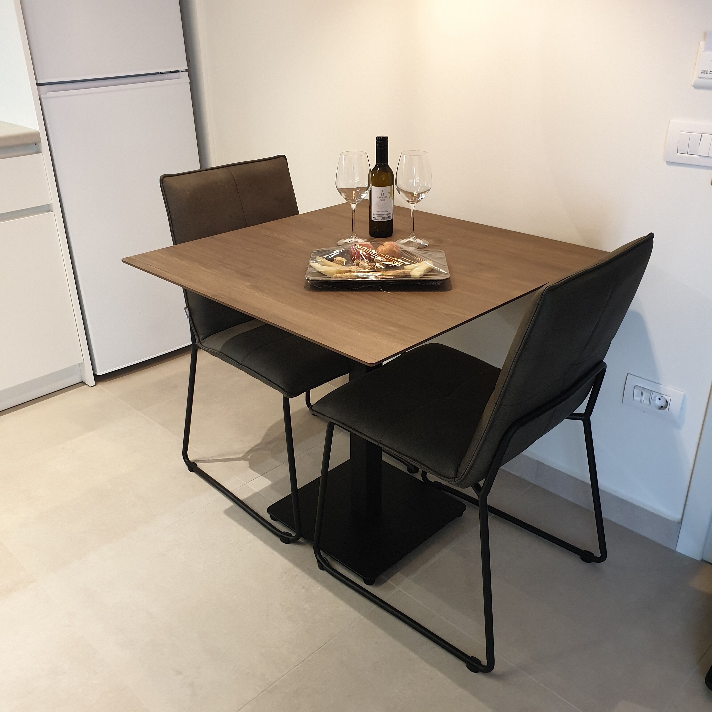 A dining table with two chairs, a bottle of wine, and two wine glasses.