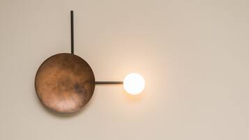 A wall-mounted light fixture with a circular shade and a straight rod.