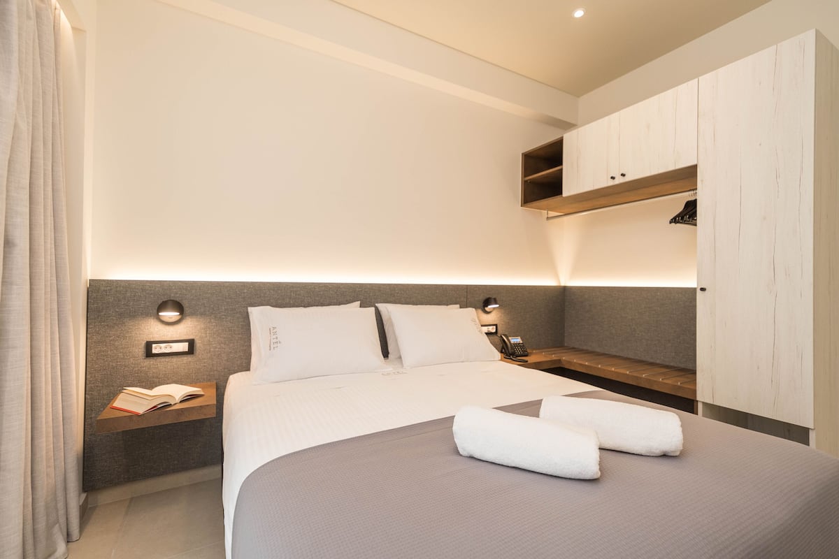 A modern hotel room with a large bed, bedside tables, a built-in wardrobe, and a bedside lamp.