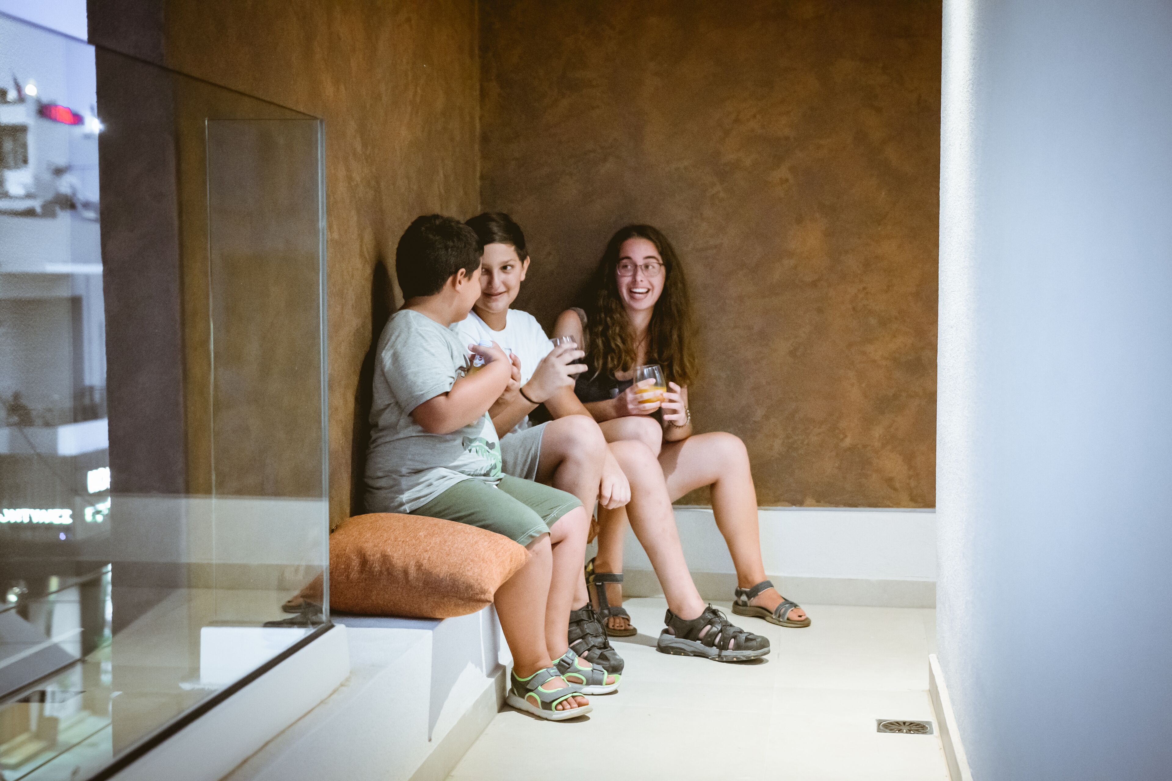 Three people sitting on a bench in a modern interior with a glass partition and a white floor.