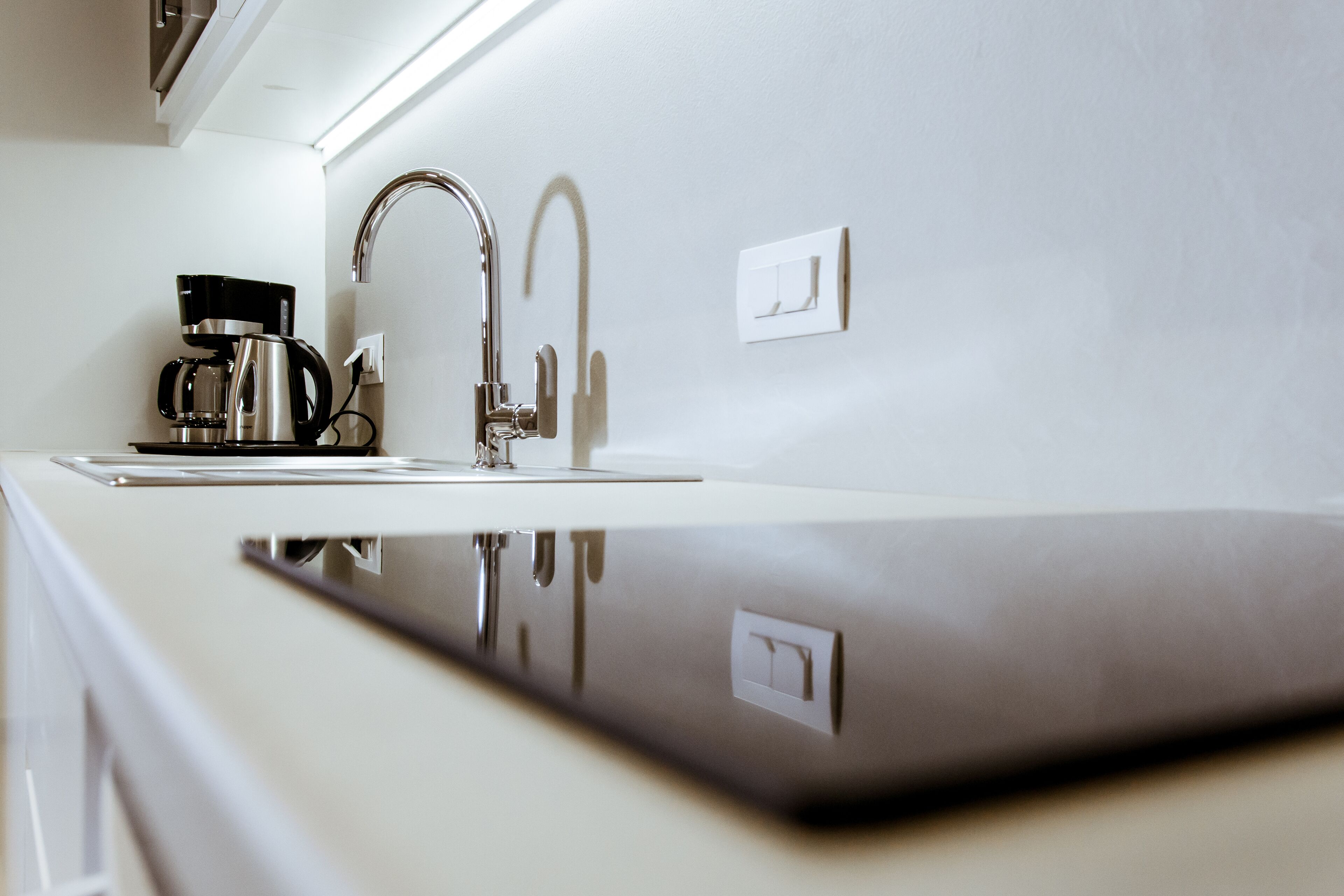 Una cucina moderna con una macchina da caffè in acciaio inossidabile, un rubinetto e un interruttore a parete.