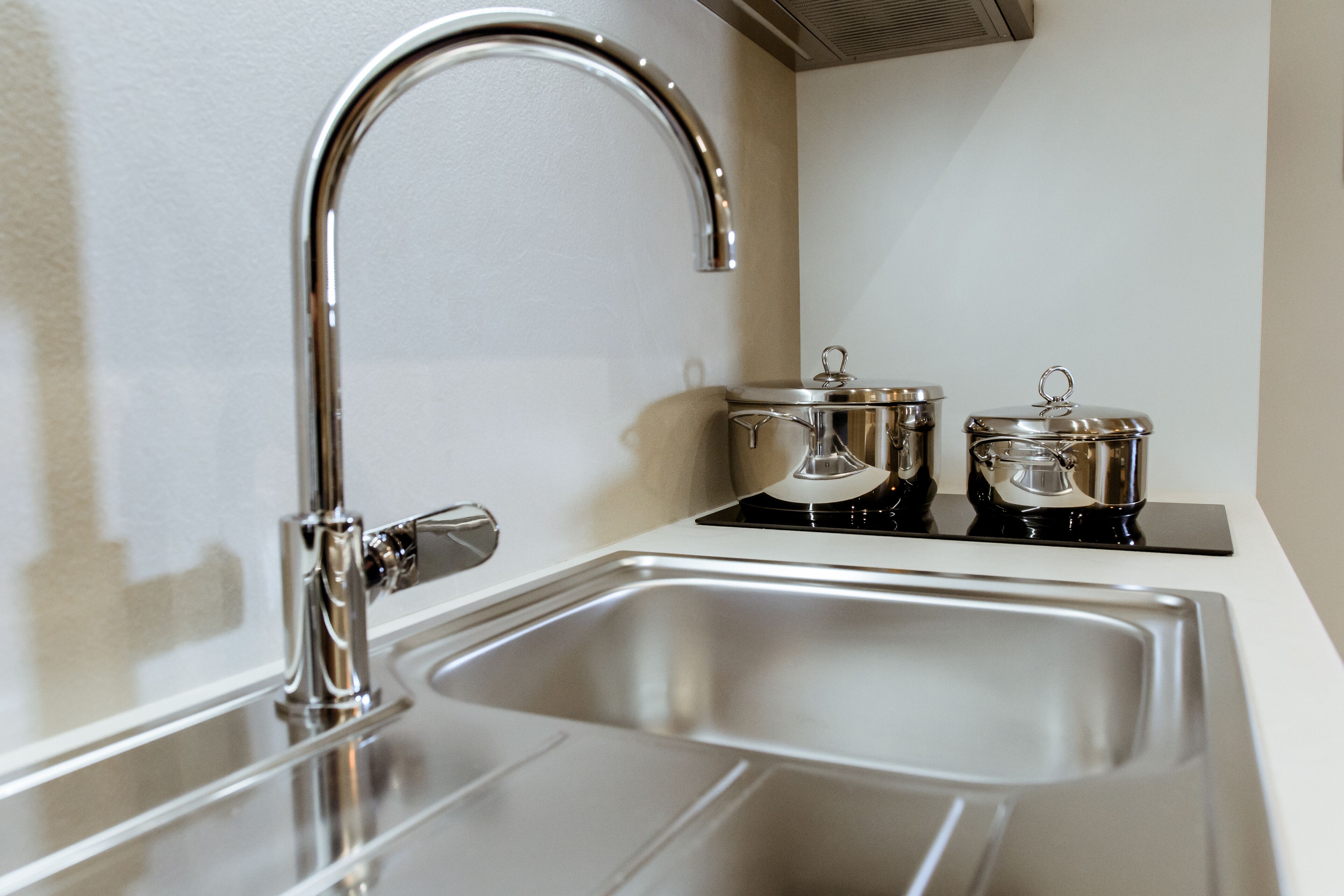 Eine moderne Küche mit einer Spüle aus Edelstahl, einem Wasserhahn und zwei Töpfen auf der Arbeitsfläche.