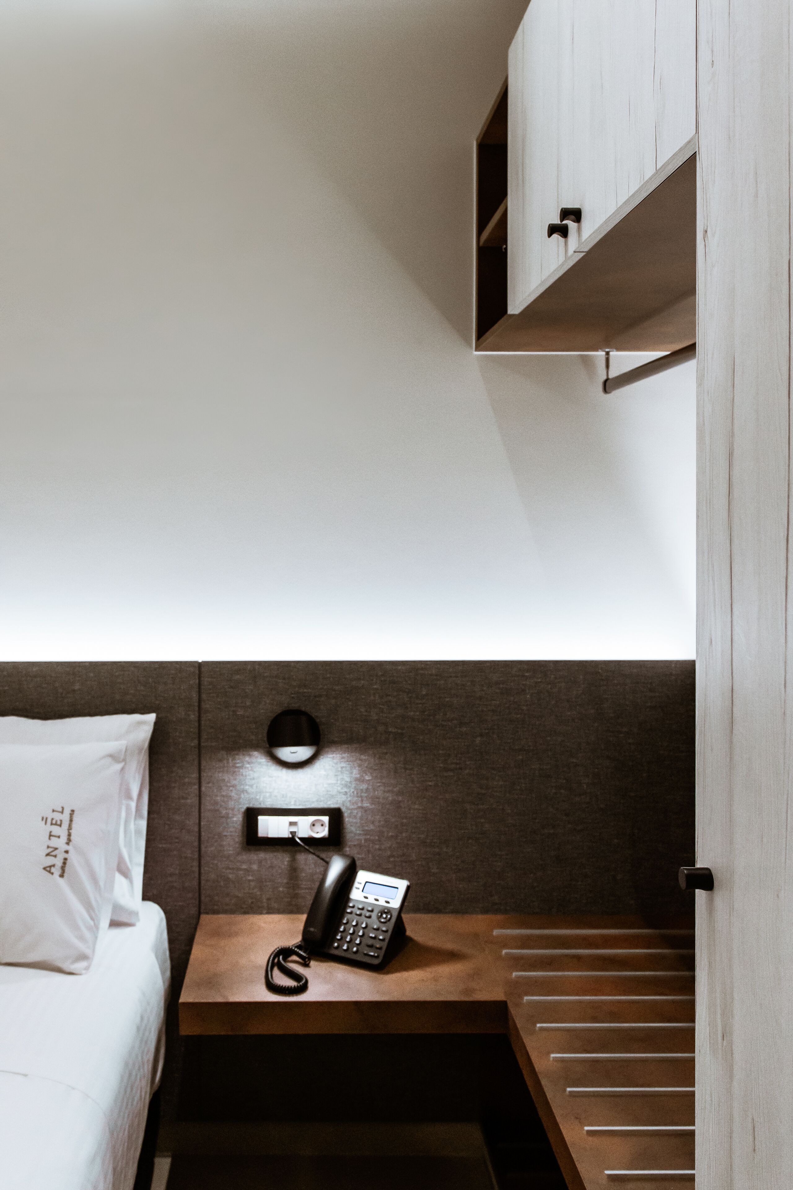 Une chambre d’hôtel avec un lit, une table de chevet avec un téléphone et une étagère en bois au-dessus du lit.