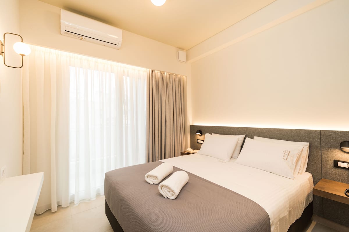 A hotel room with a bed, curtains, a nightstand, and a wall-mounted air conditioner.