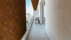 A narrow balcony with a view of the city, a tiled floor, and a row of chairs.