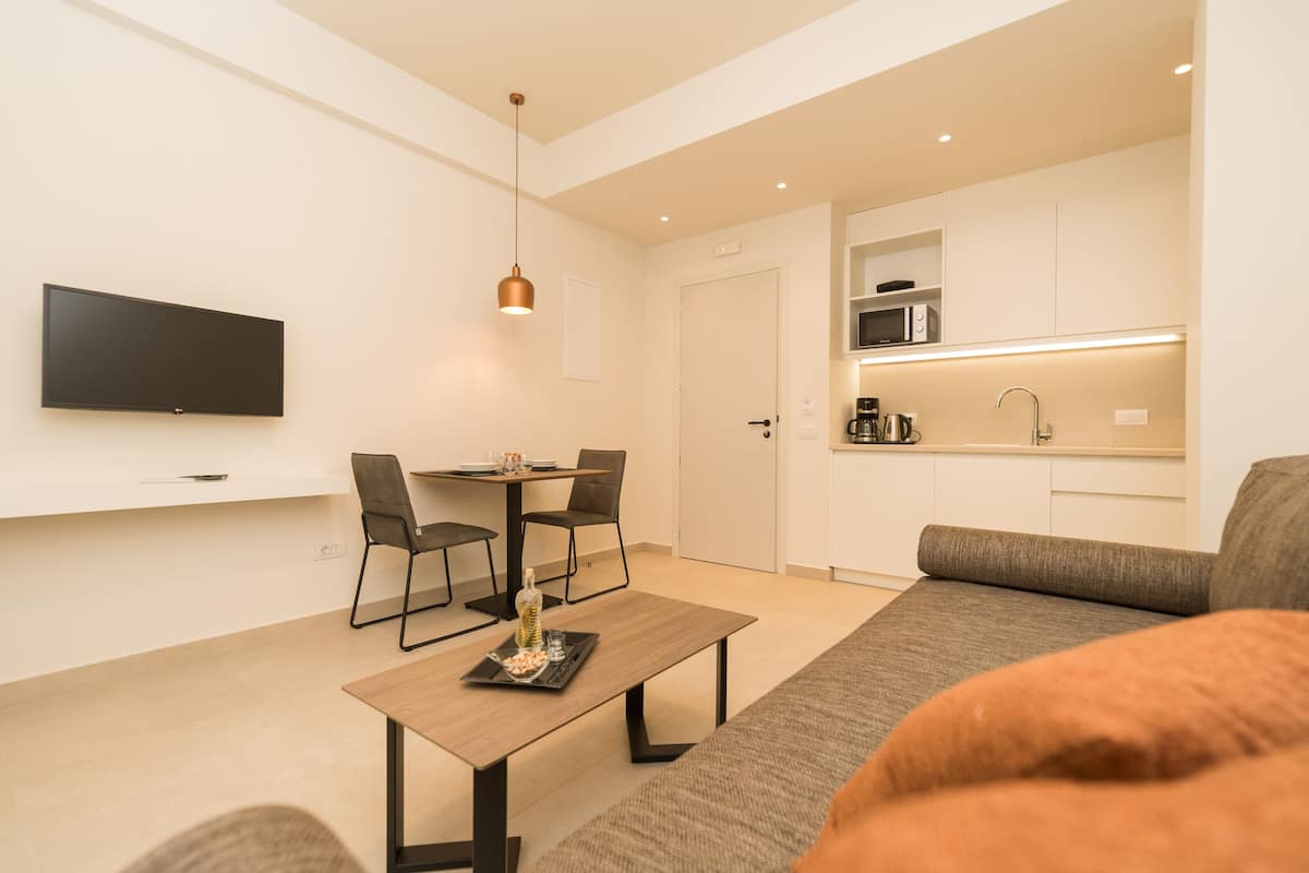A modern living room with a flat-screen TV, a dining area with a table and chairs, a kitchen with a microwave, and a sofa.