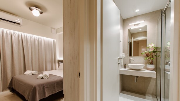 A modern bathroom with a glass shower, a large mirror, and a sink with a vase of flowers.