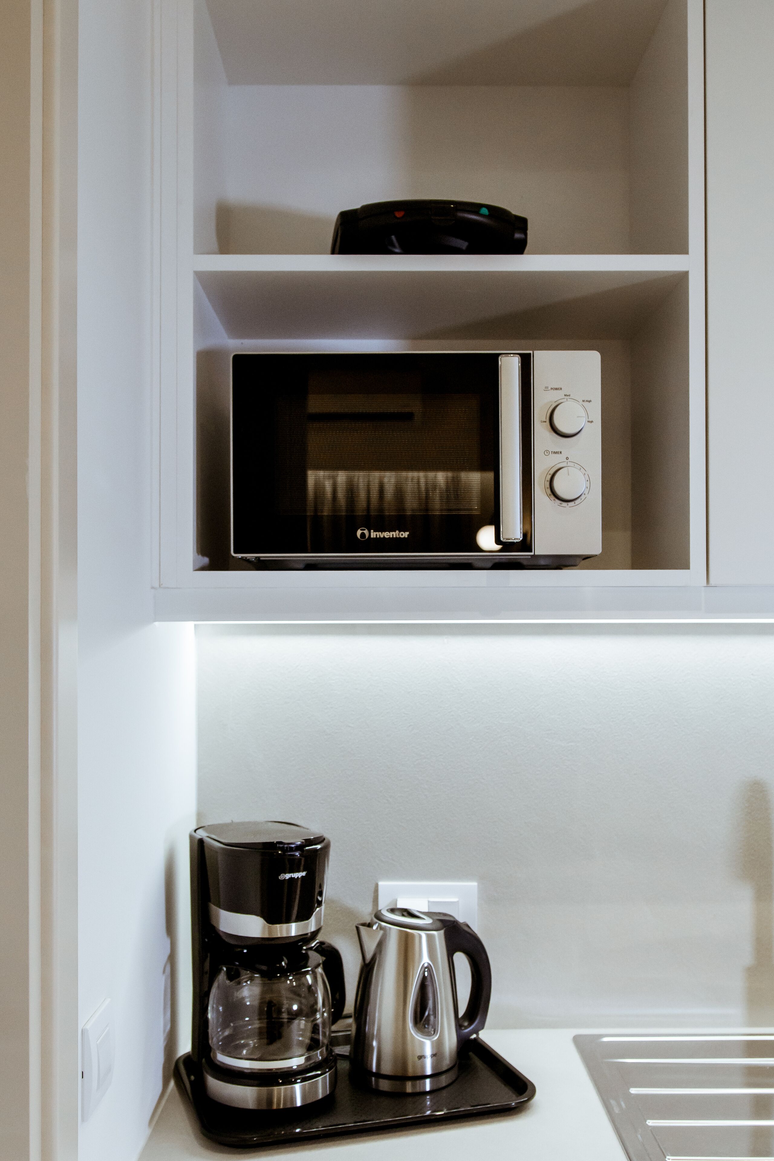 A kitchen with a microwave on a white shelf, a coffee maker, and a kettle on the counter.