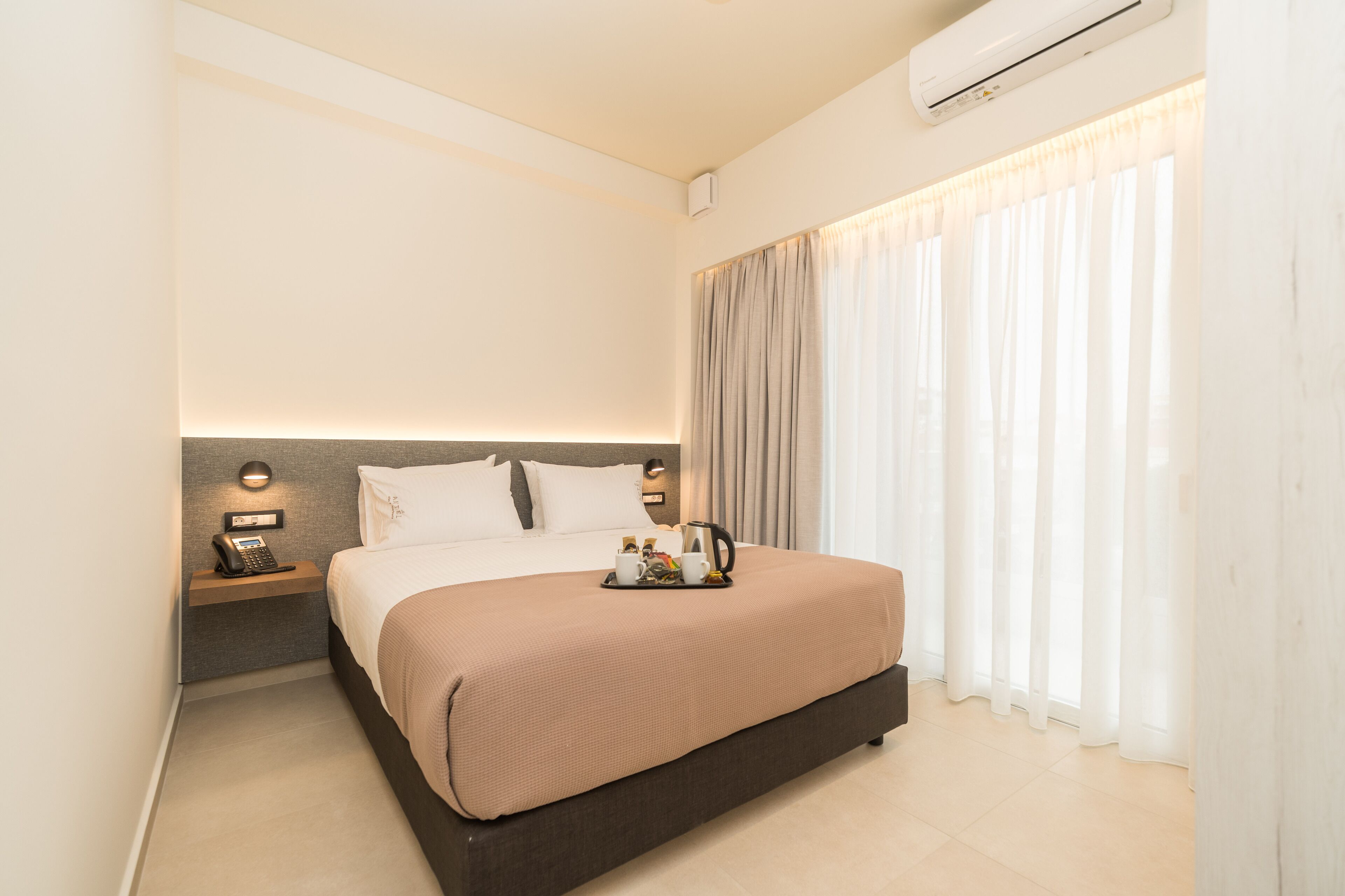 Una habitación de hotel moderna con una cama grande, una mesita de noche con un teléfono y una bandeja con tazas y una tetera.
