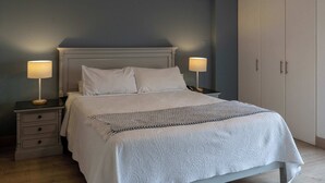 Ein ordentlich bezogenes Bett mit weißen Leinen, zwei Nachttische mit Lampen sowie ein Kleiderschrank mit Schiebetüren.