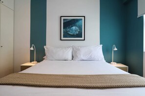 A neatly made bed with white linens, two bedside lamps, and a framed artwork above it. - w* | Amazing 2BR near Malecon in Miraflores (Miraflores)