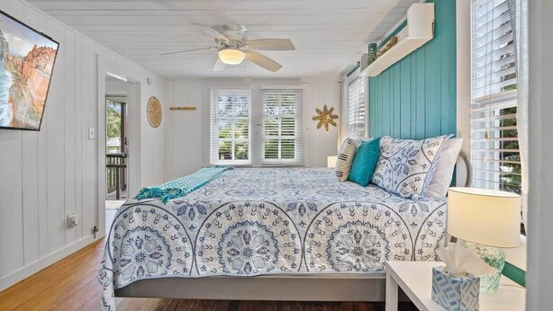 A bedroom with a bed, a ceiling fan, a window with blinds, and a wall-mounted clock. - Marvelous Mermaid Beach Bungalow, Dog-Friendly (St. Augustine)