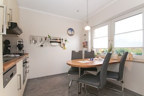 A modern kitchen with a wooden table and chairs, a coffee machine, and various utensils hanging on the wall.