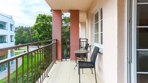 A balcony with a table and chairs, a railing, and a view of a green area and a building. - Apartamenty Swinoujscie - Villa Park (Swinoujscie)