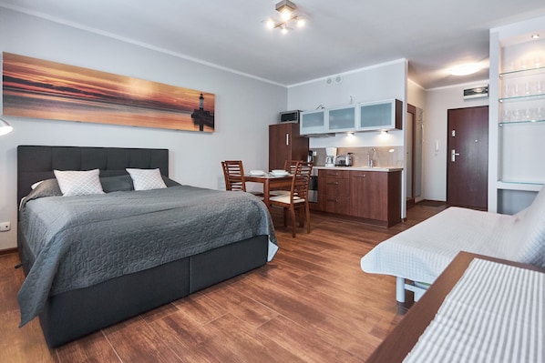 A compact room with a bed, a small dining table, a kitchenette, and a glass display cabinet.
