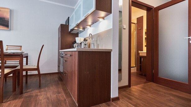 A compact kitchen with wooden cabinets, a dining table with chairs, and a view into the adjacent bathroom. - Apartamenty Swinoujscie - Villa Park (Swinoujscie)