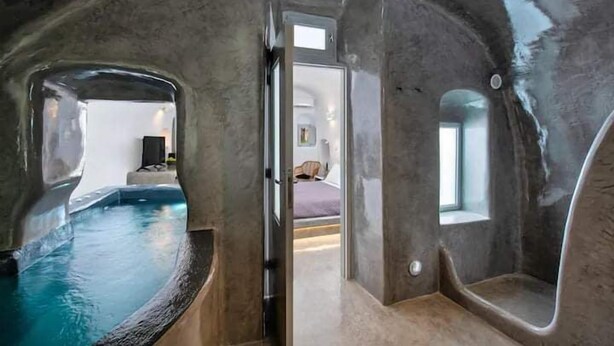 A room with a large bathtub, a door leading to another room, and a small window. - Aetheria Villas (Santorini)