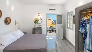 A bedroom with a bed, bedside table, and a view of an outdoor area with a table and chairs. - Aetheria Villas (Santorini)