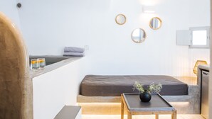 A modern, minimalist room with a sofa, a small table with a vase, and three wall-mounted mirrors. - Aetheria Villas (Santorini)