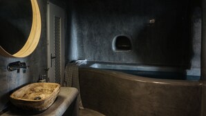 A bathroom with a wooden basin, a round mirror, and a bathtub. - Aetheria Villas (Santorini)