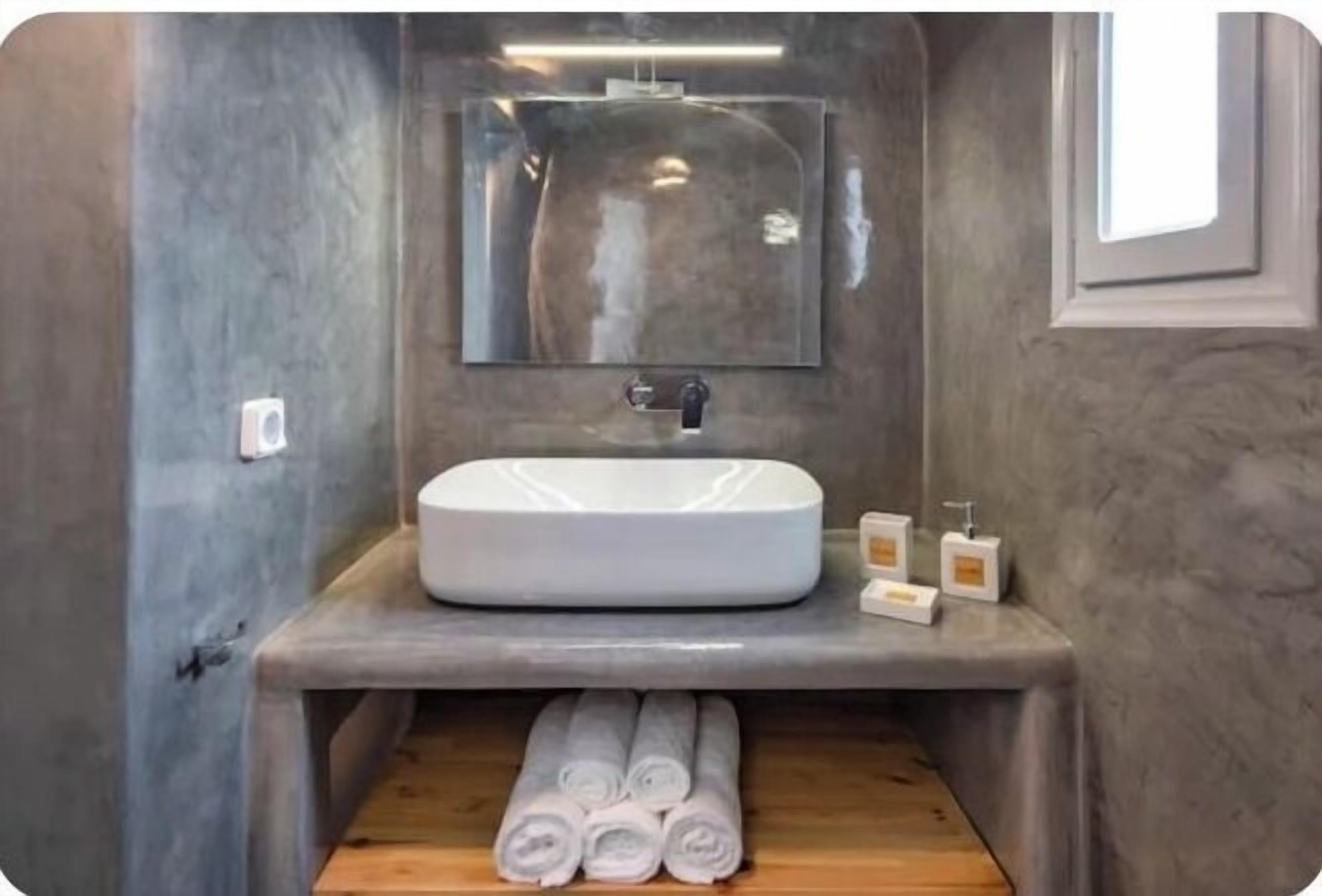 A bathroom with a white sink, mirror, and wooden floor. There are towels and toiletries on the counter.
