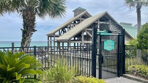 A beach pavilion entrance with a sign, surrounded by palm trees and a view of the ocean. - Steps to Pvt beach/Beach ramp/2 pools/Sleeps 18 (Miramar Beach)