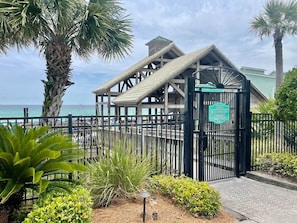 A beach pavilion entrance with a sign, surrounded by palm trees and a view of the ocean.